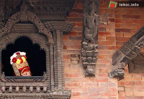 Một đứa trẻ trong trang phục nữ thần Kumari Devi đang nhìn qua ô cửa trước khi bước vào lễ hội Indrajatra tại Kathmandu. Cộng đồng Newar của Nepal thường tổ chức lễ hội Indrajatra để cầu thánh Kumari và cầu thần mưa Indra.